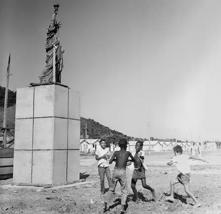 Estátua da Liberdade em preto e branco, com crianças brincando ao fundo.