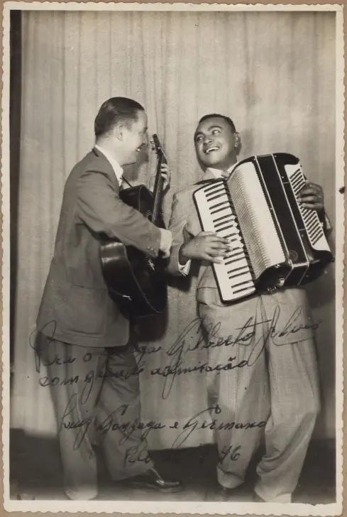 Dois homens em ternos clássicos apresentando música, um com violão e o outro com acordeon.