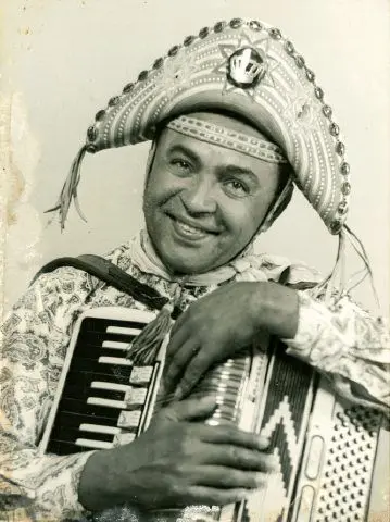 Homem com chapéu de penas segurando acordeon.
