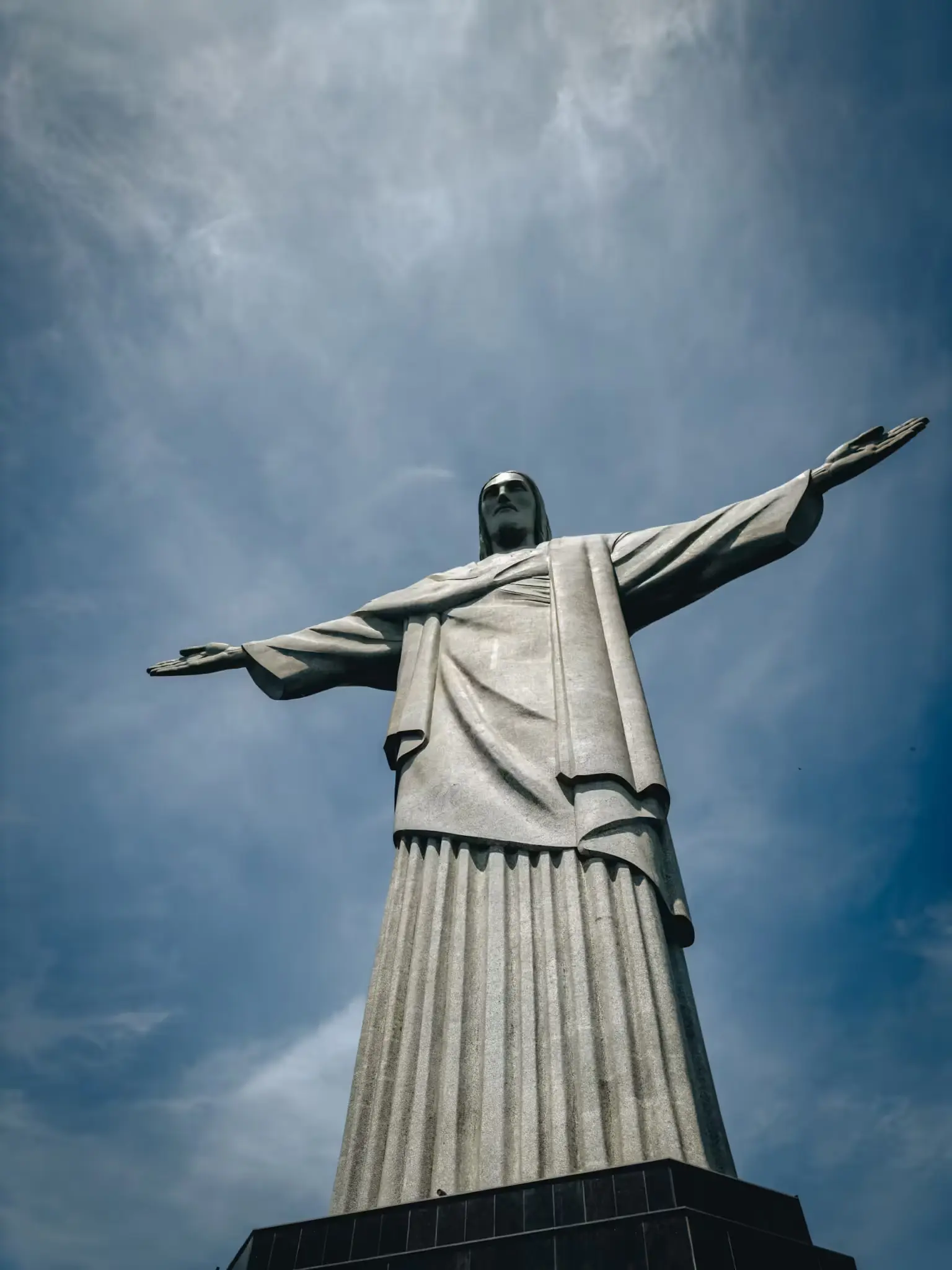 Monumento Cristo Redentor, céu azul e nuvens ao fundo.