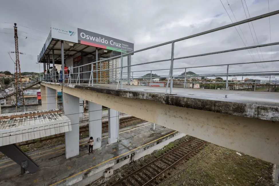 Plataforma elevada em estação ferroviária com sinal "Oswaldo Cruz" e pessoas esperando.