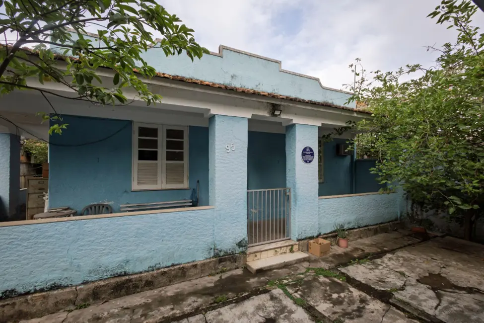 Casa azul clara com detalhes brancos, árvore e arbustos ao ar livre.