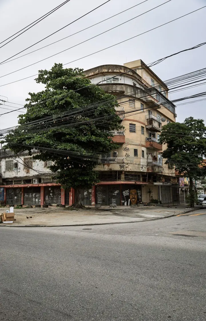 Prédio residencial com árvores e lojas fechadas, céu nublado.