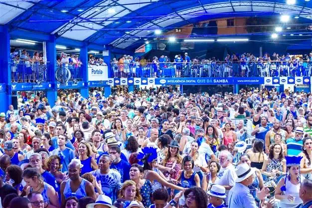 Multidão em evento cultural sambista, com pessoas vestindo azul e branco.