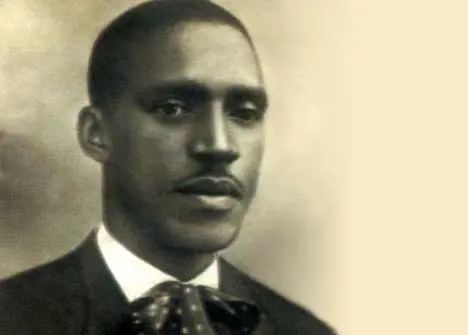 Homem em terno preto com gravata borboleta, foto em preto e branco.