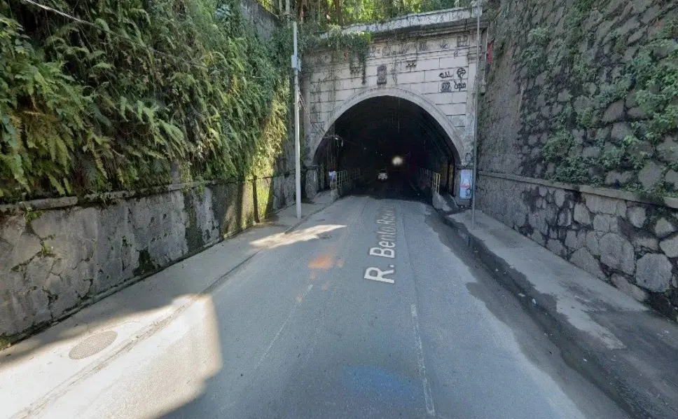Túnel com vegetação e placa na entrada.