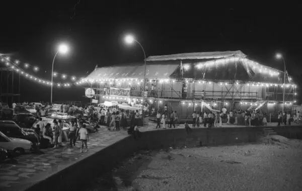 Circo noturno com palco iluminado e pessoas caminhando.