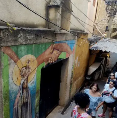 Pessoas caminhando em um ambiente urbano com pintura religiosa à esquerda.