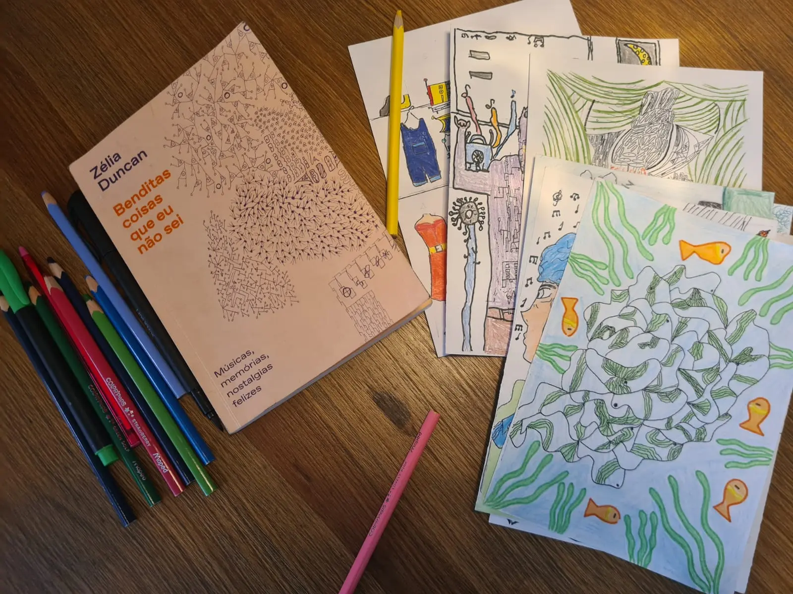 Objetos escolares sobre madeira, incluindo caderno, lápis e folhas de papel coloridas.