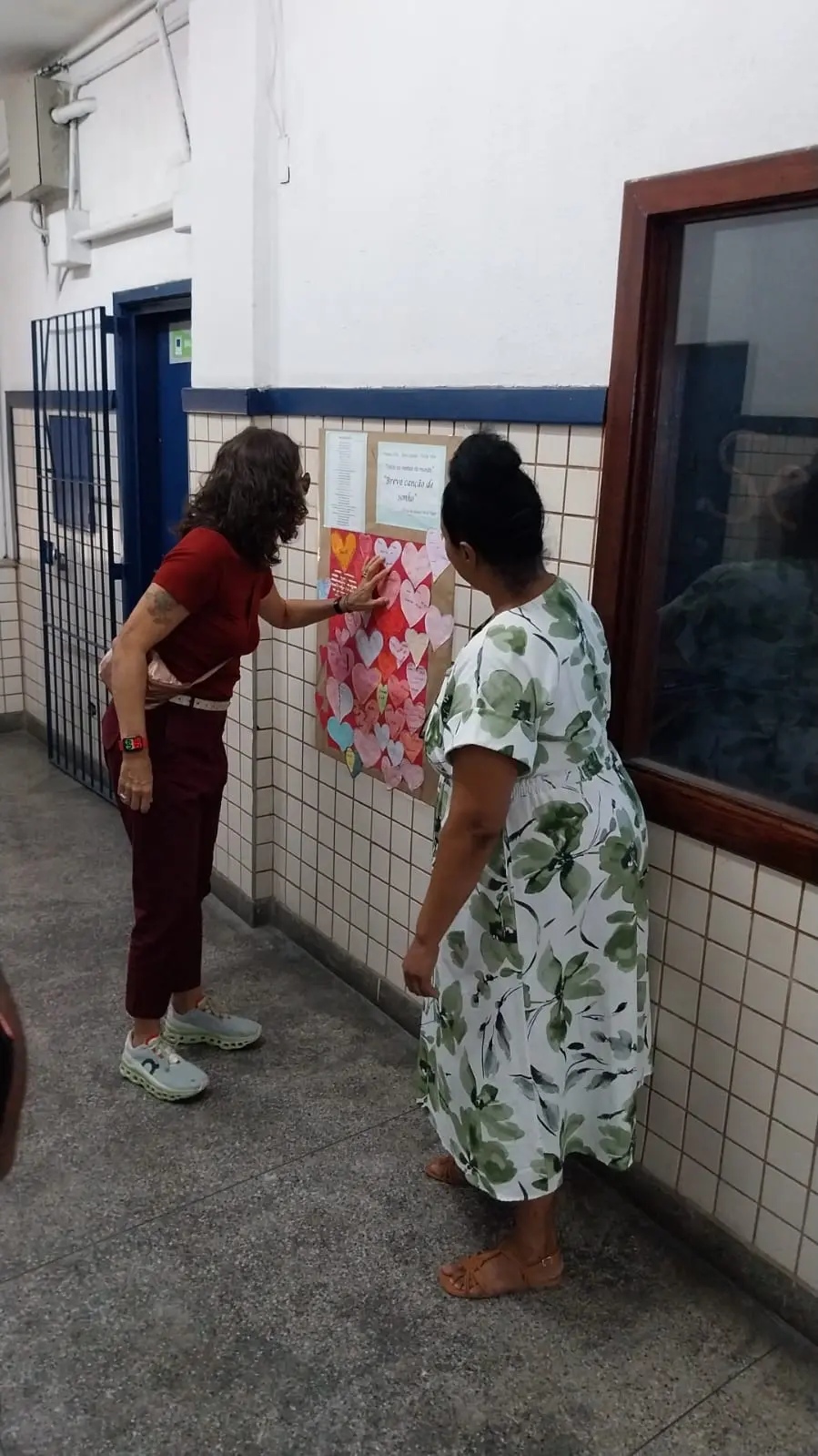 Duas mulheres interagem com um cartaz de corações coloridos pendurado na parede.