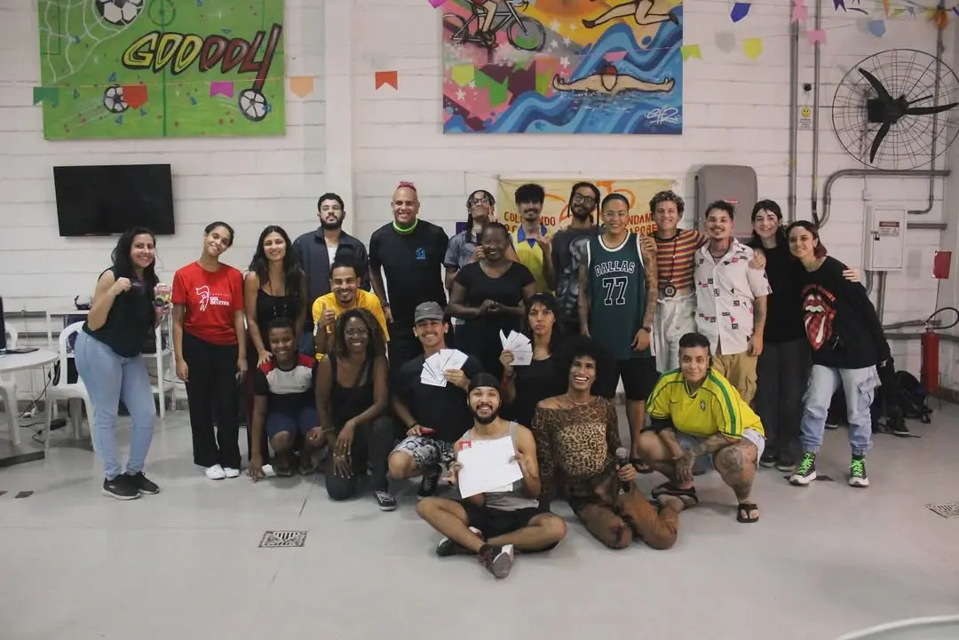 Um grupo de pessoas celebra em um ambiente escolar com faixas coloridas e ventilador.