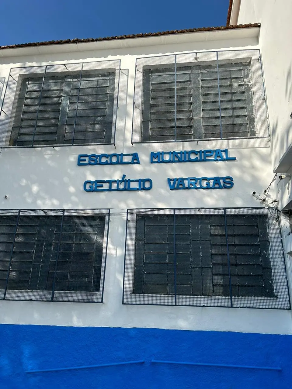 Fachada de escola municipal com telhado vermelho e janelas grandes.