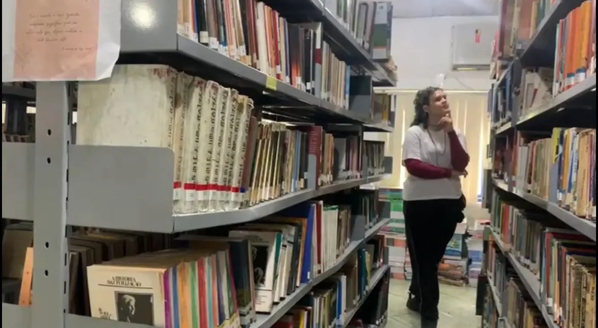 Biblioteca com prateleiras cinza repletas de livros.