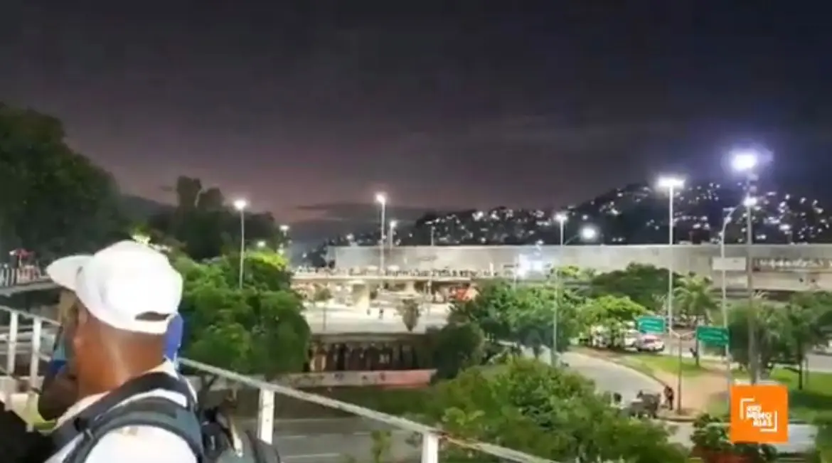 Fotografia noturna urbana com pessoa, escada, árvores, estrada e construção iluminada.