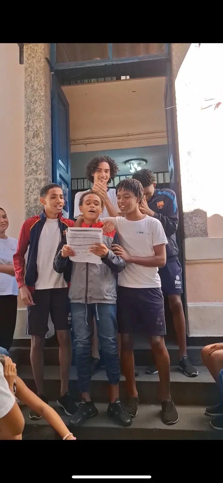 Crianças sorridentes em frente à escola, segurando papel.
