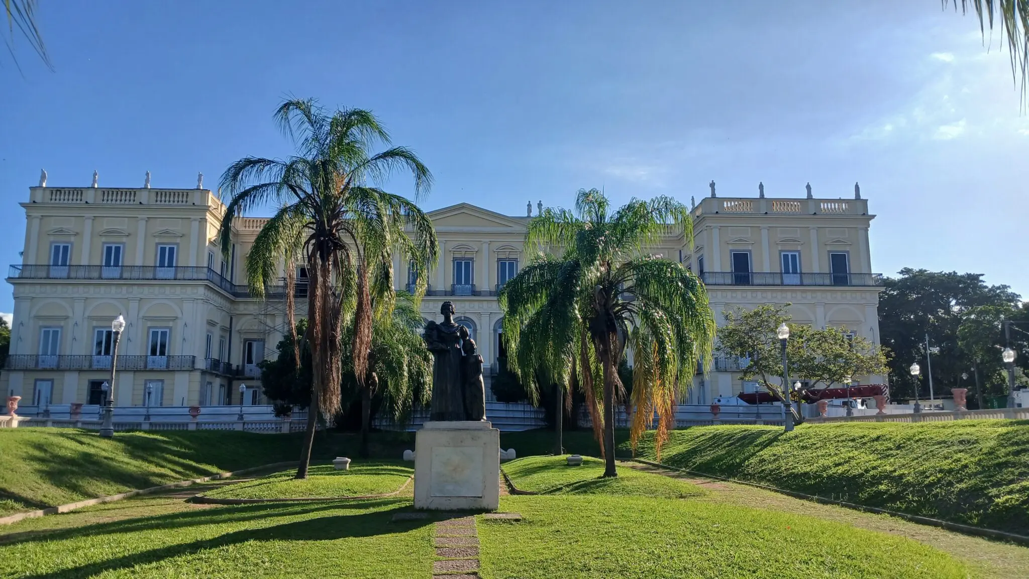 Palácio clássico com palmeiras e estátuas.