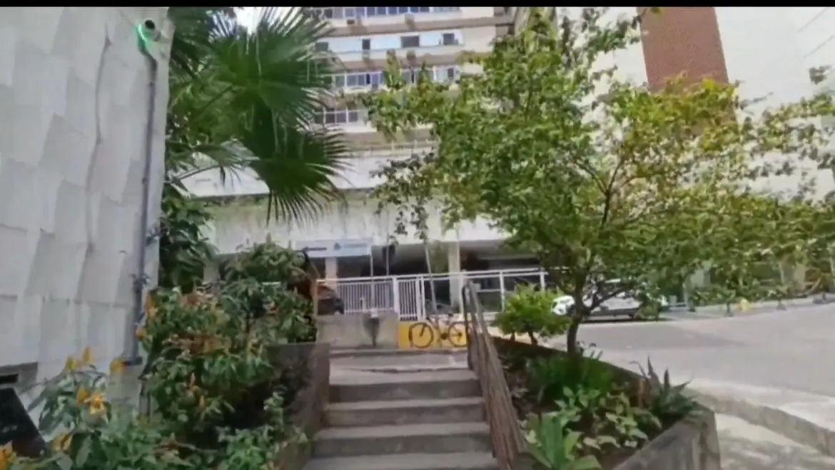 Prédio residencial com câmera de segurança, escadaria, árvores e entrada aberta.