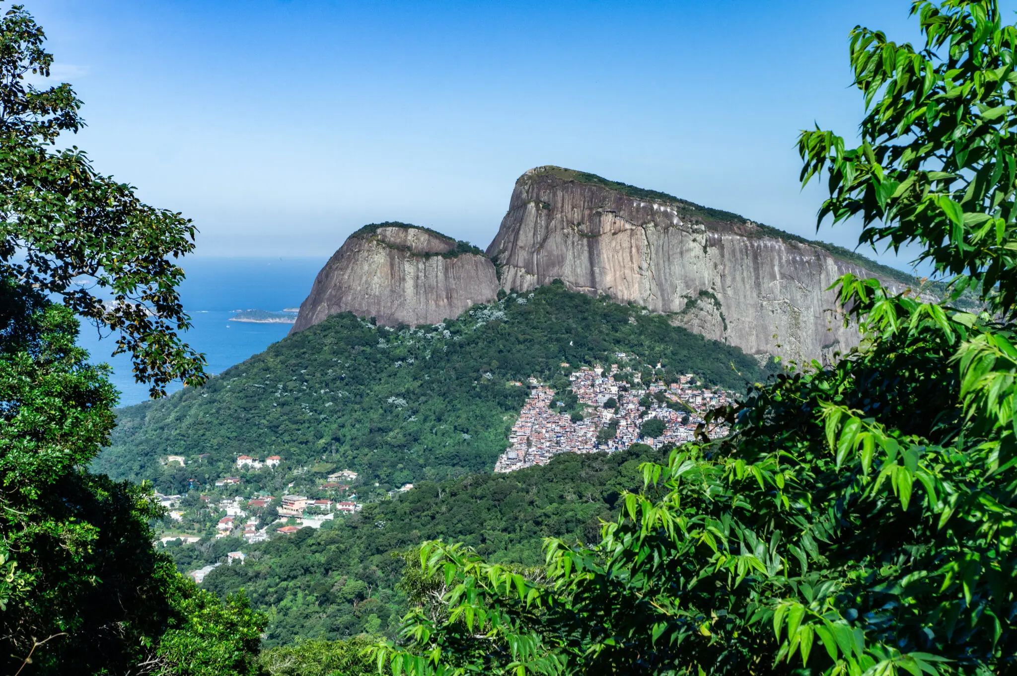 Montanha com vegetação densa, casas coloridas nas encostas, mar azul ao fundo.