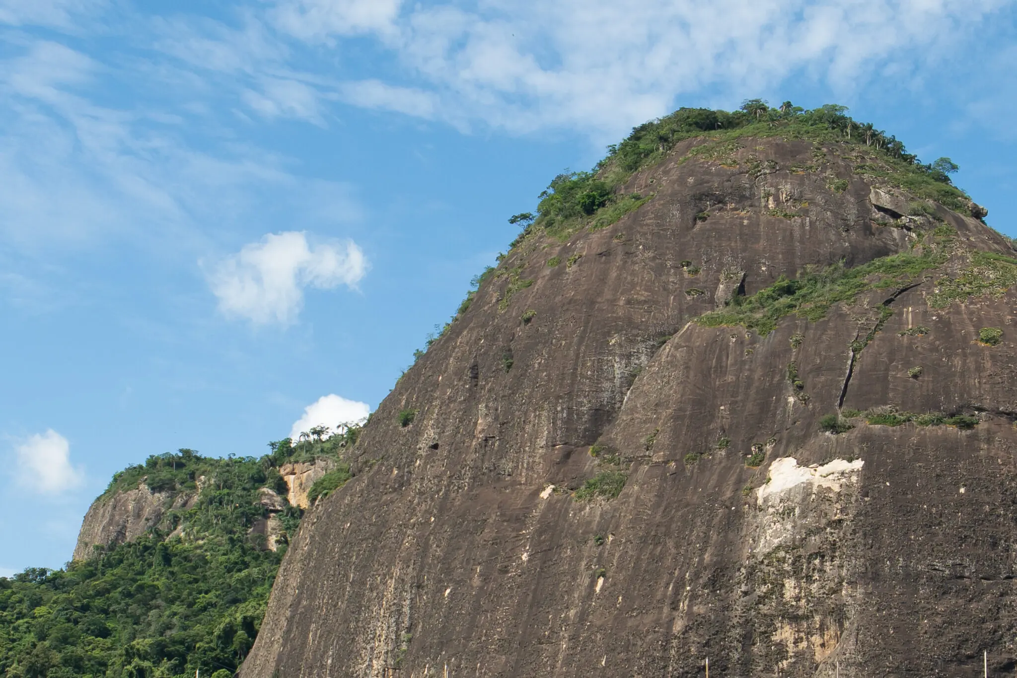 Maciço rochoso sob céu azul com vegetação verde.
