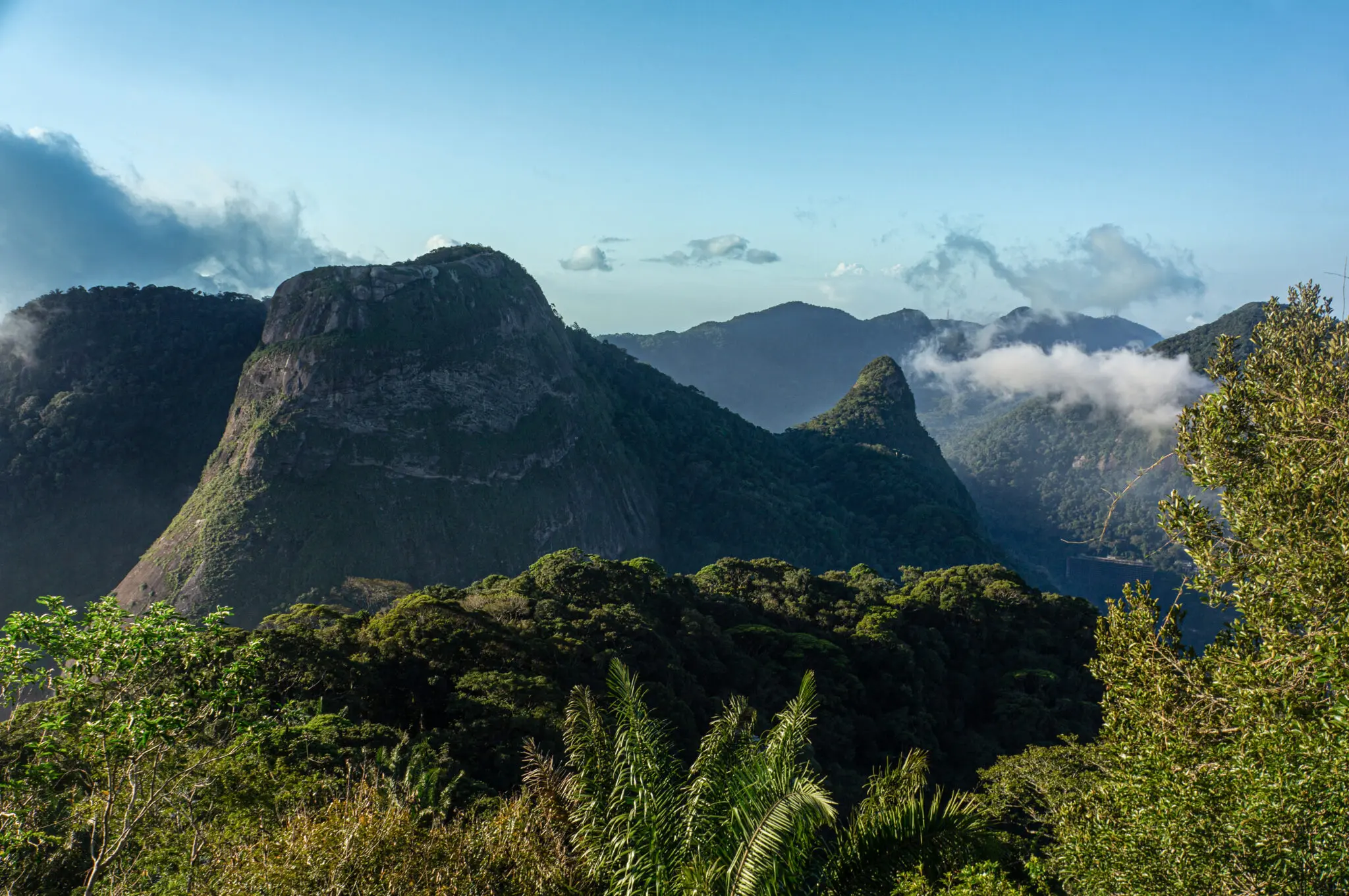 Maciço montanhoso com vegetação verde e céu azul claro.