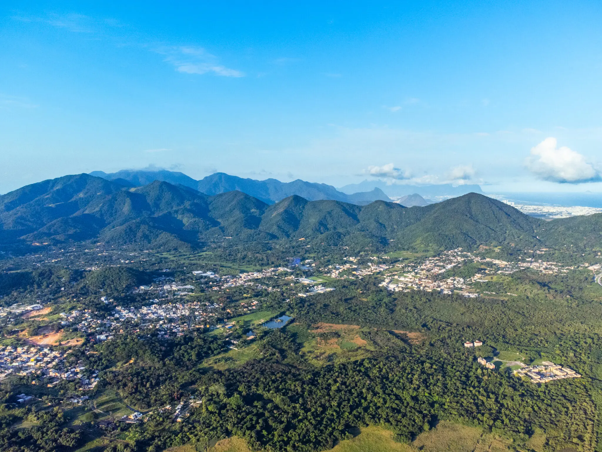 Maciço montanhoso com vegetação verde, área urbana densa e lago pequeno.