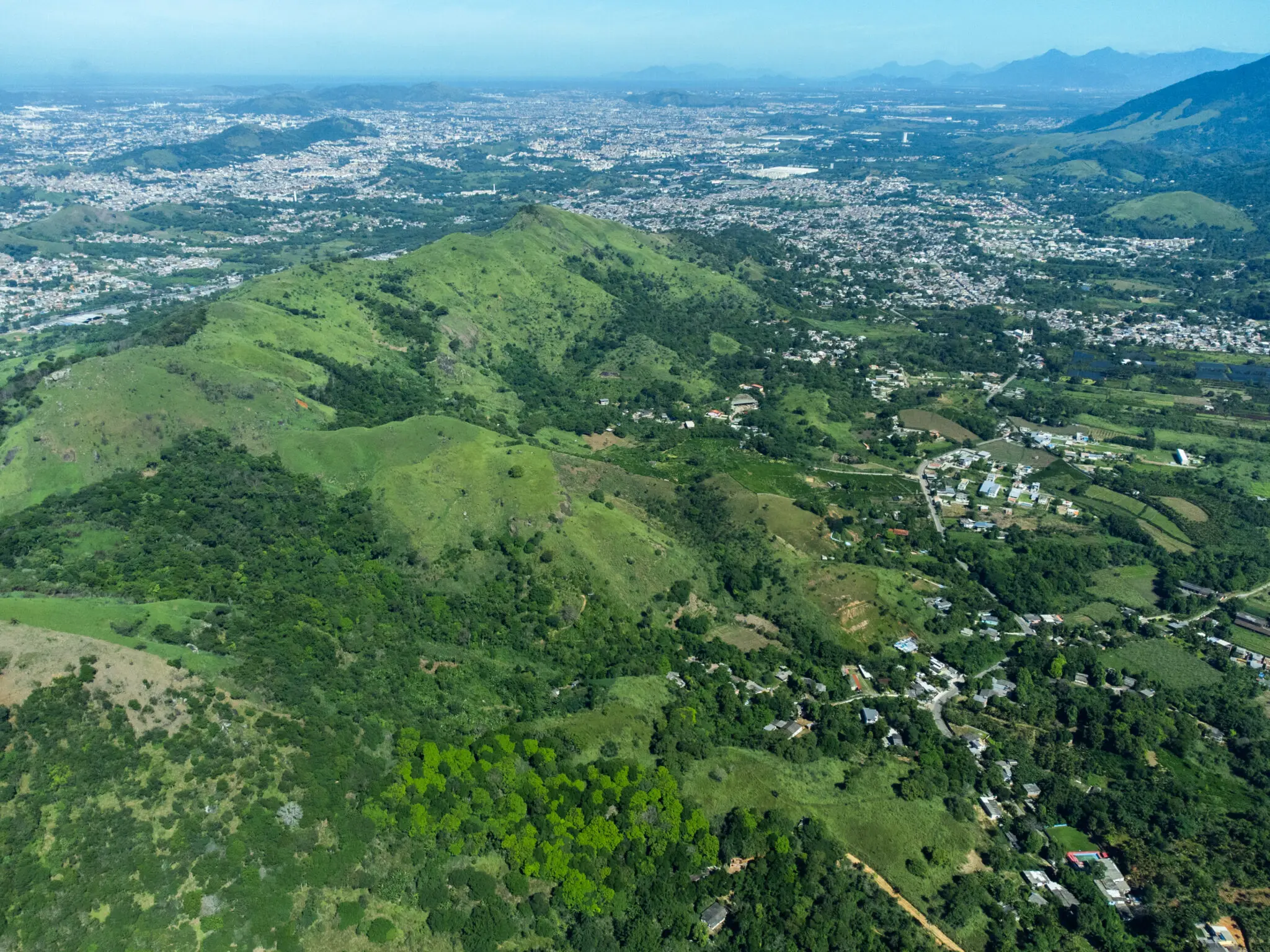 Paisagem montanhosa com colinas verdes e áreas urbanizadas.