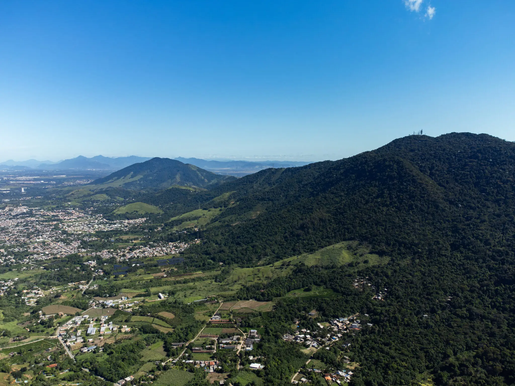 Maciço montanhoso sob céu azul claro, com cidade densa à esquerda e vegetação verde à direita.