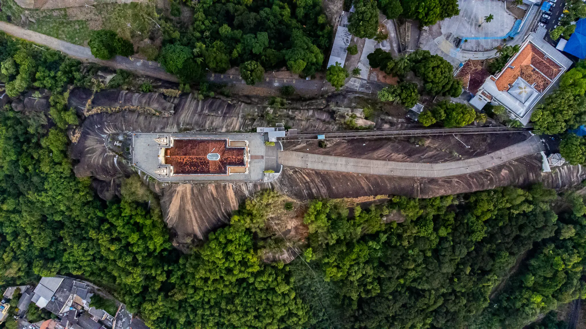 Área montanhosa com vegetação verde, edifício vermelho e estrada.