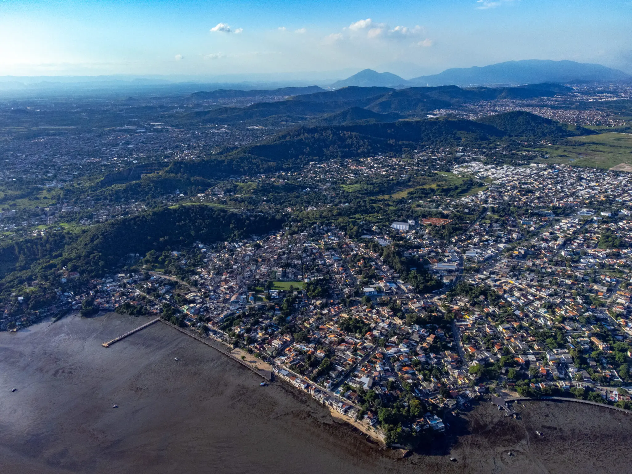 Cidade costeira em península rodeada por água e montanhas verdes.