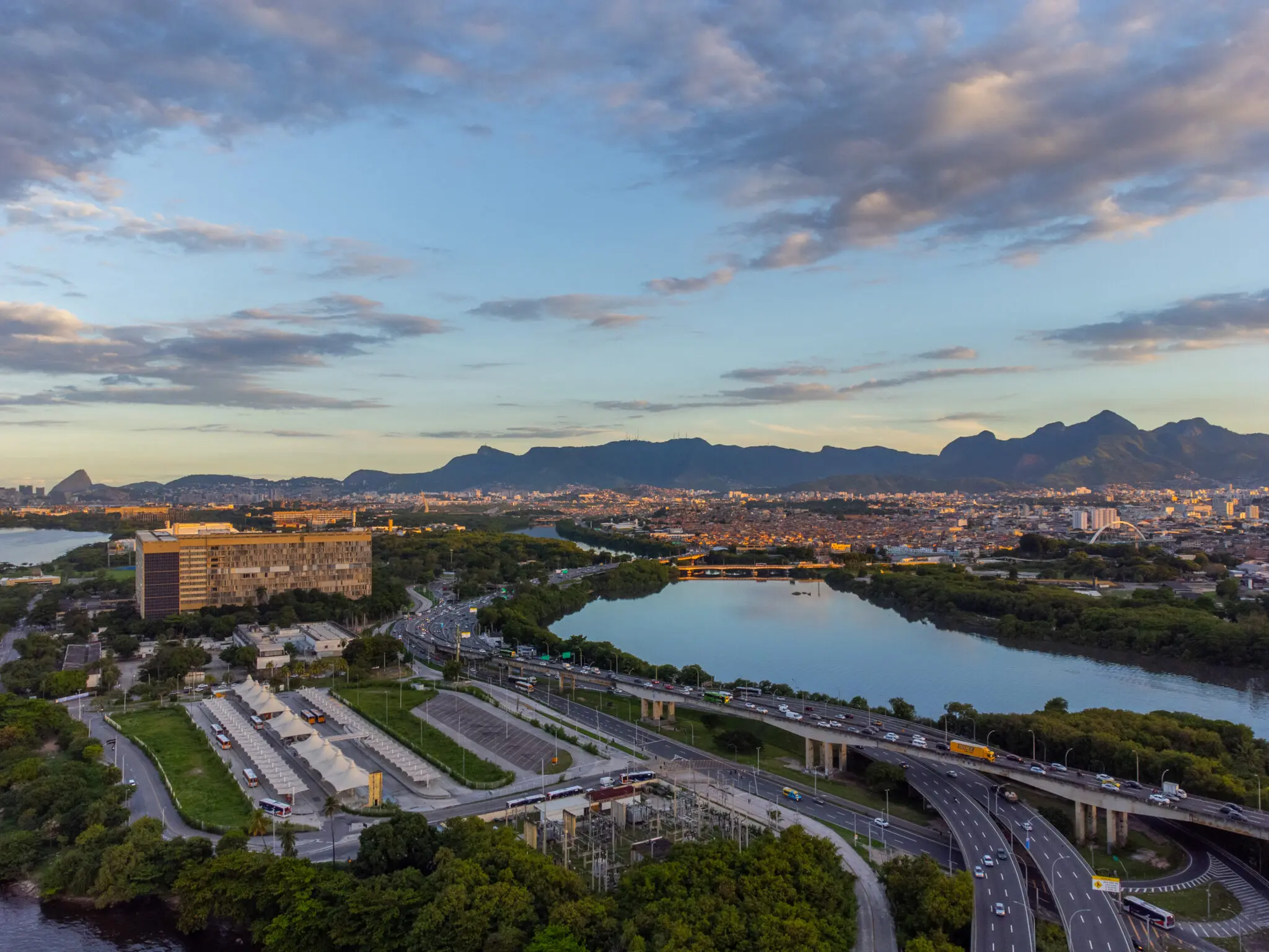 Paisagem urbana durante o crepúsculo com edifício moderno, estrada movimentada, rio e cidade densa.