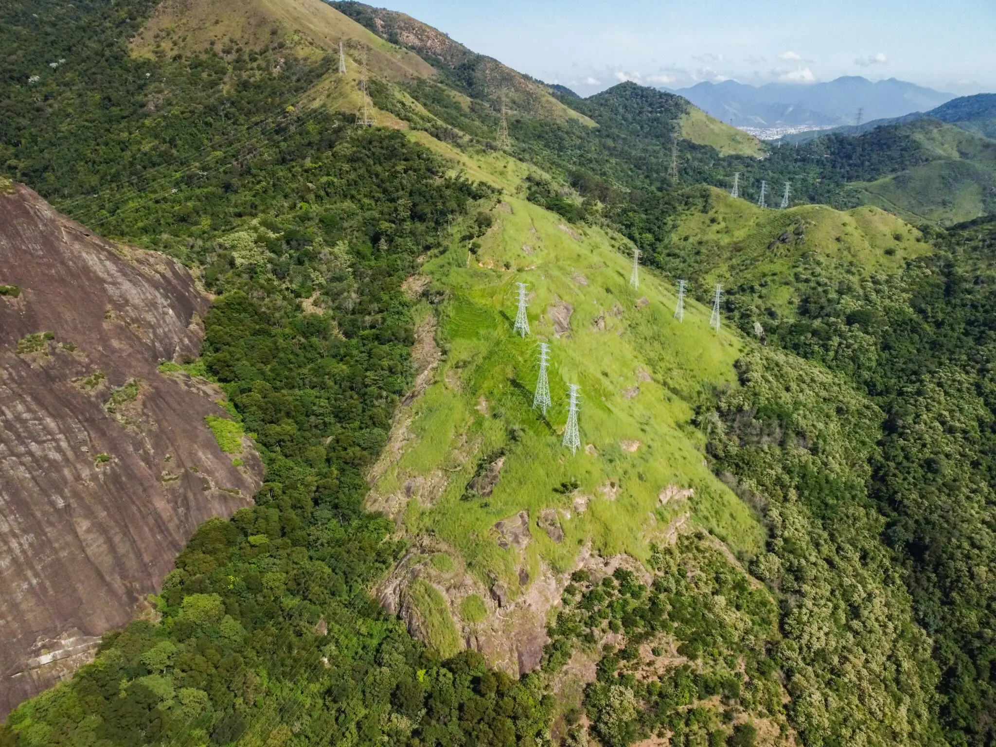 Paisagem montanhosa com rochas, colinas verdes e estruturas elétricas.