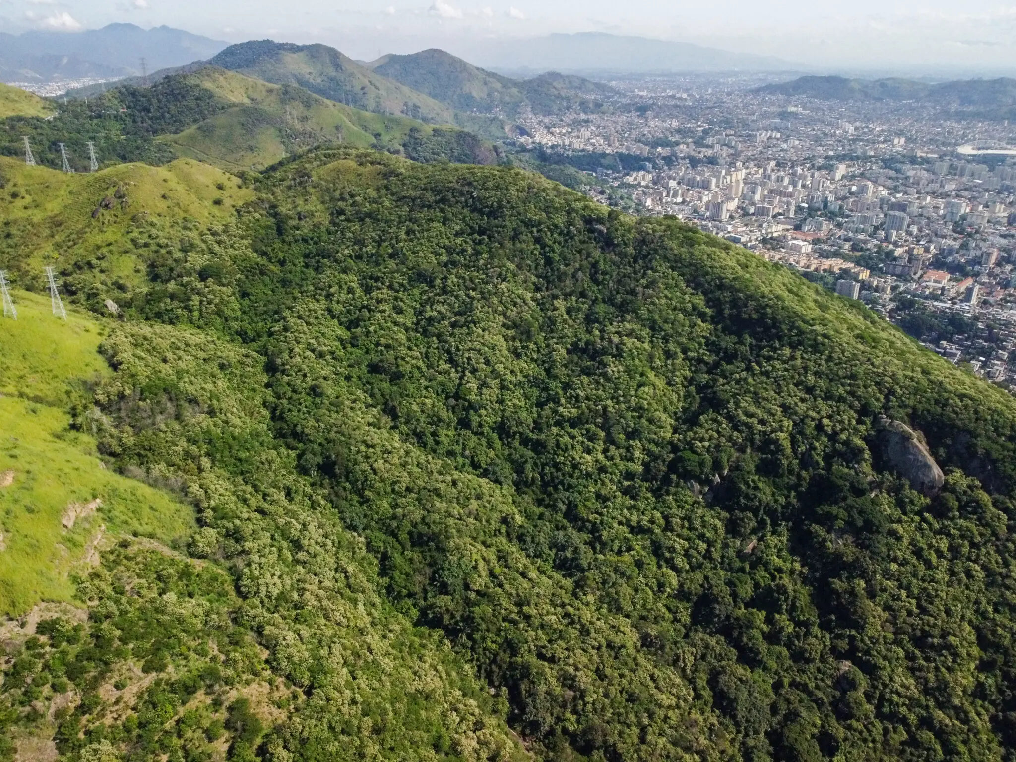 Paisagem montanhosa com vegetação variada e cidade ao fundo.