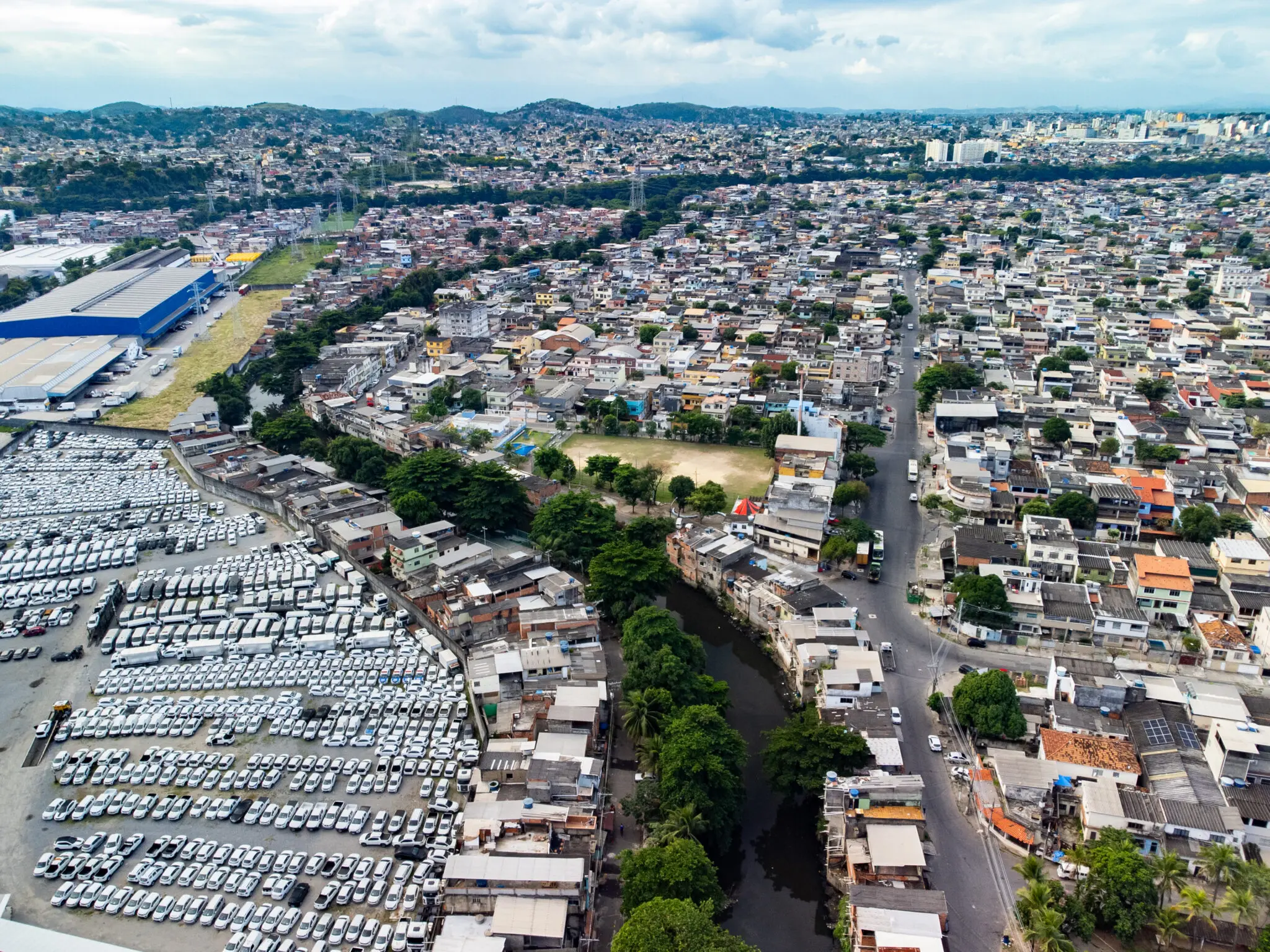 Área urbana densa com estacionamento, campo de futebol e construções próximas à estrada.