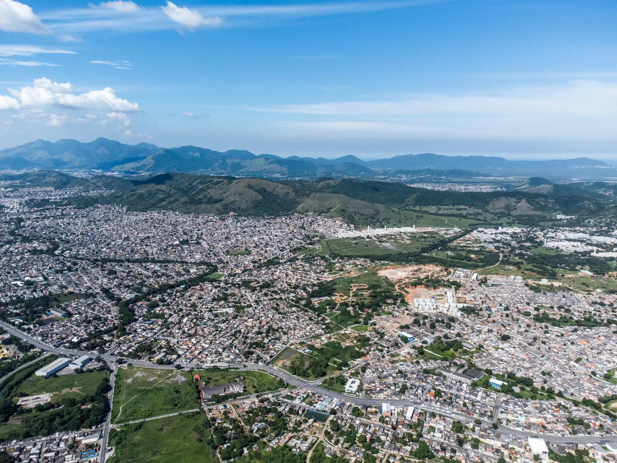 Cidade densa com áreas verdes e montanhas ao fundo.