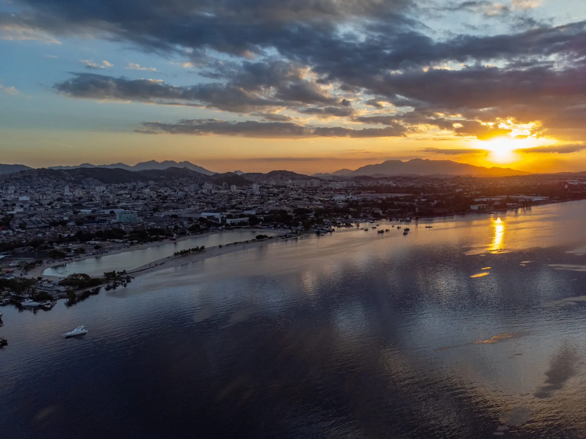Praia durante pôr-do-sol com cidade e montanhas.