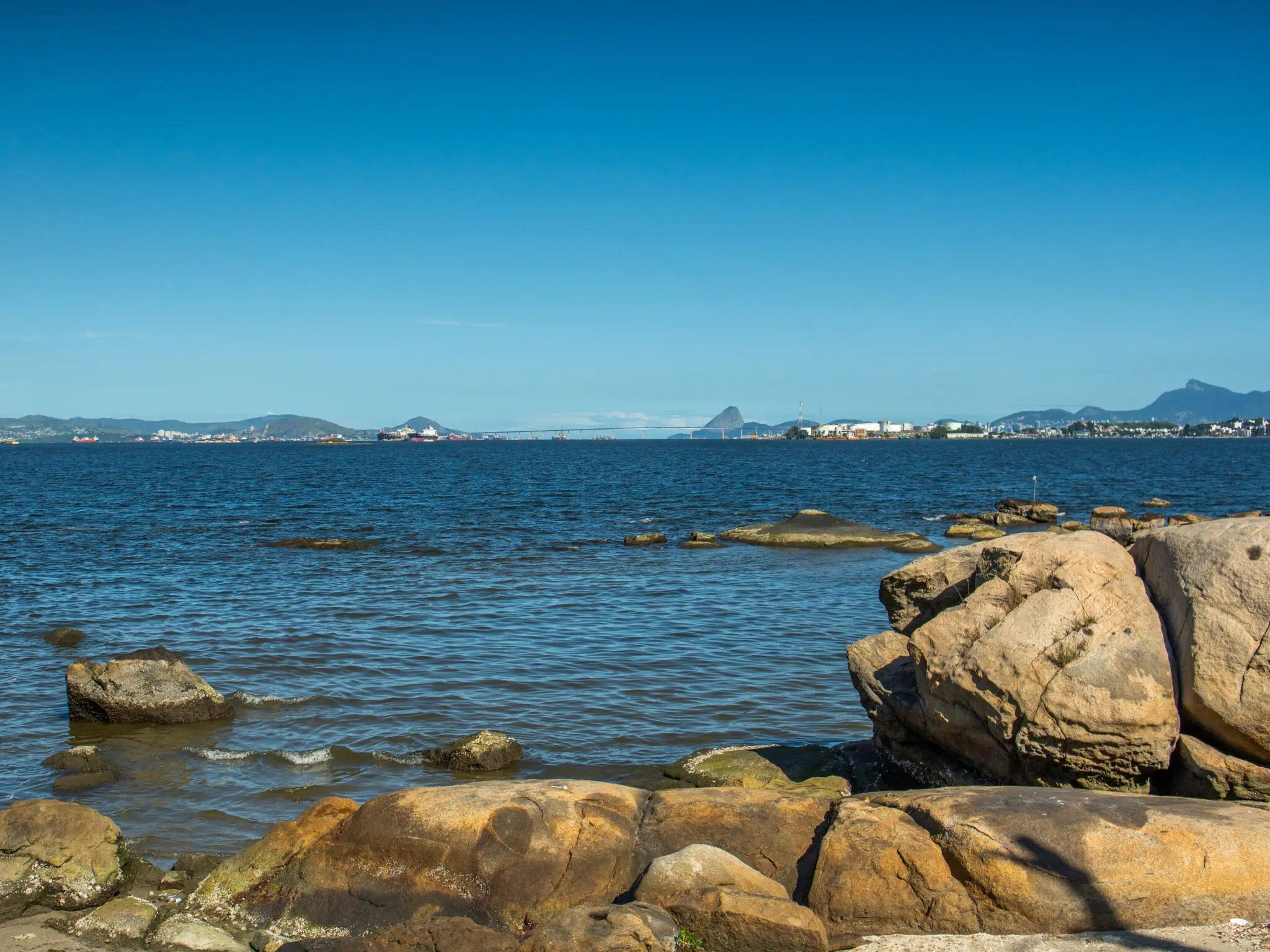 Praia com rochas, horizonte distante e água calma.