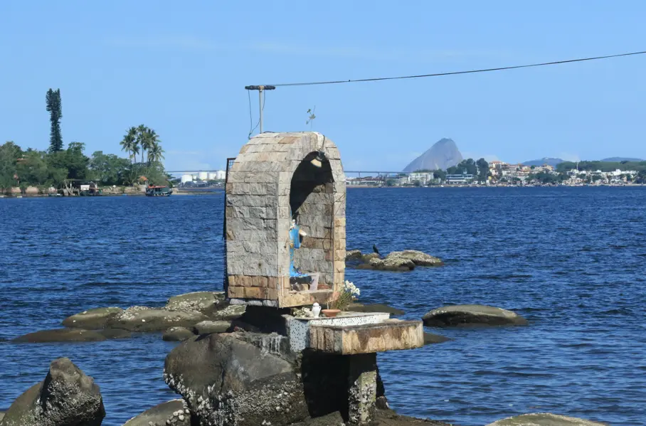 Praia com monumento, árvores, torre, mar e ilha.