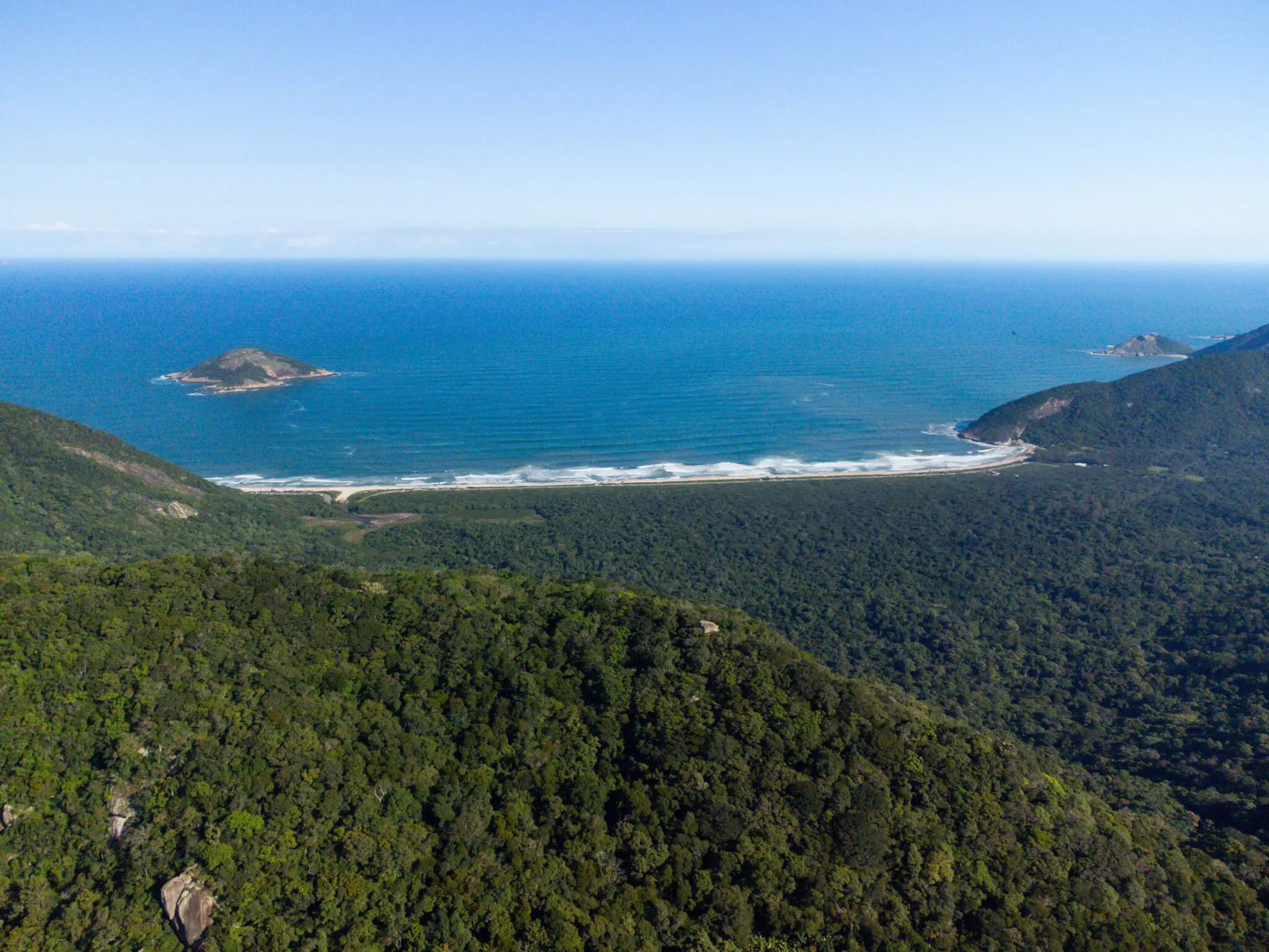 Paisagem costeira com ilha verde, praia arenosa e formação rochosa.