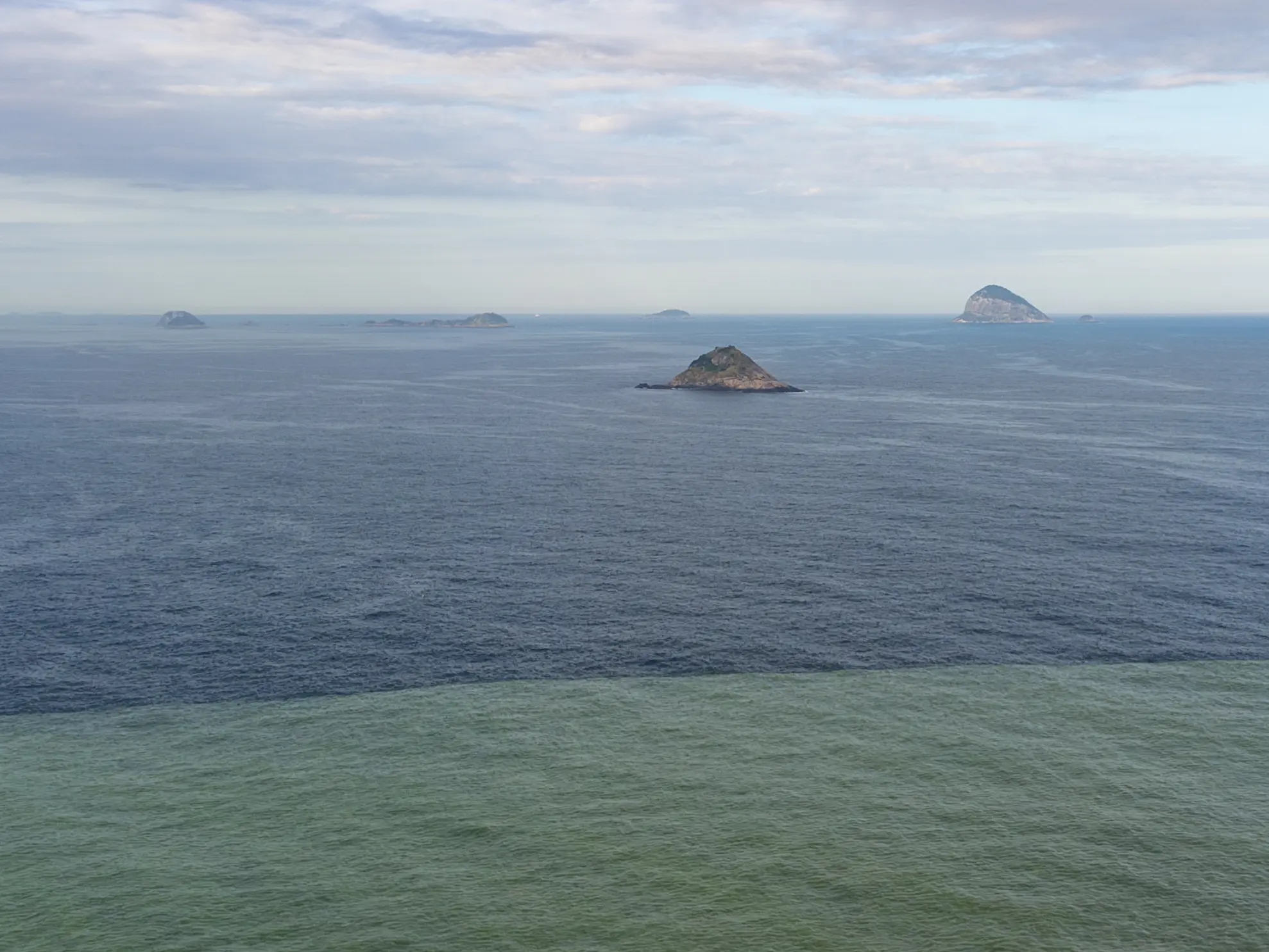Paisagem marítima com ilhas distantes e céu azul claro.