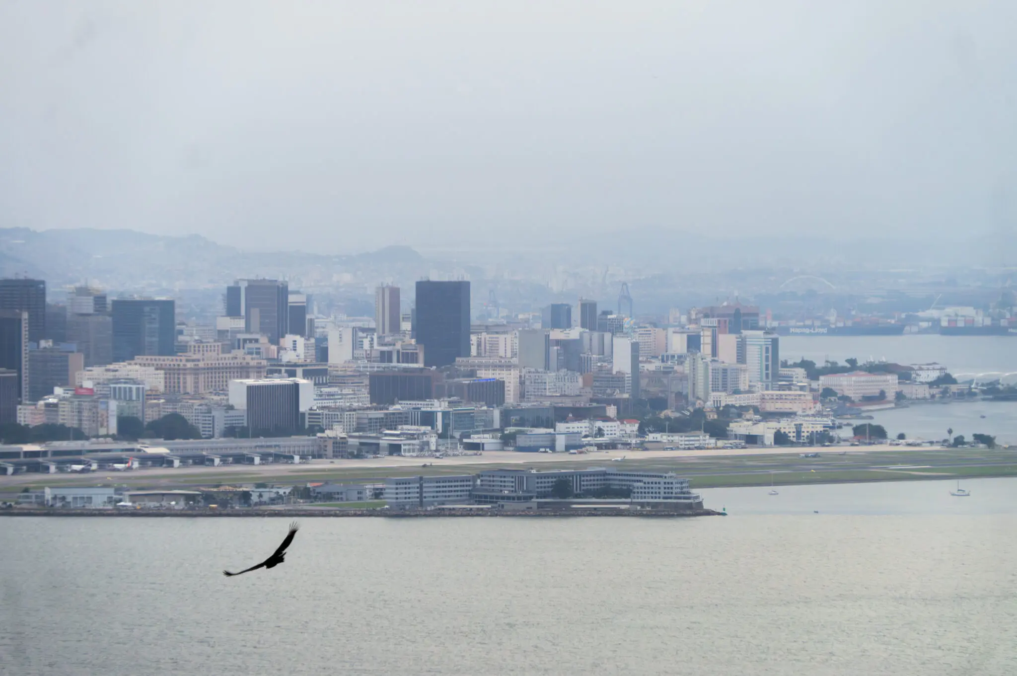 Cidade ao longo de um rio, edifícios variados e ponte.