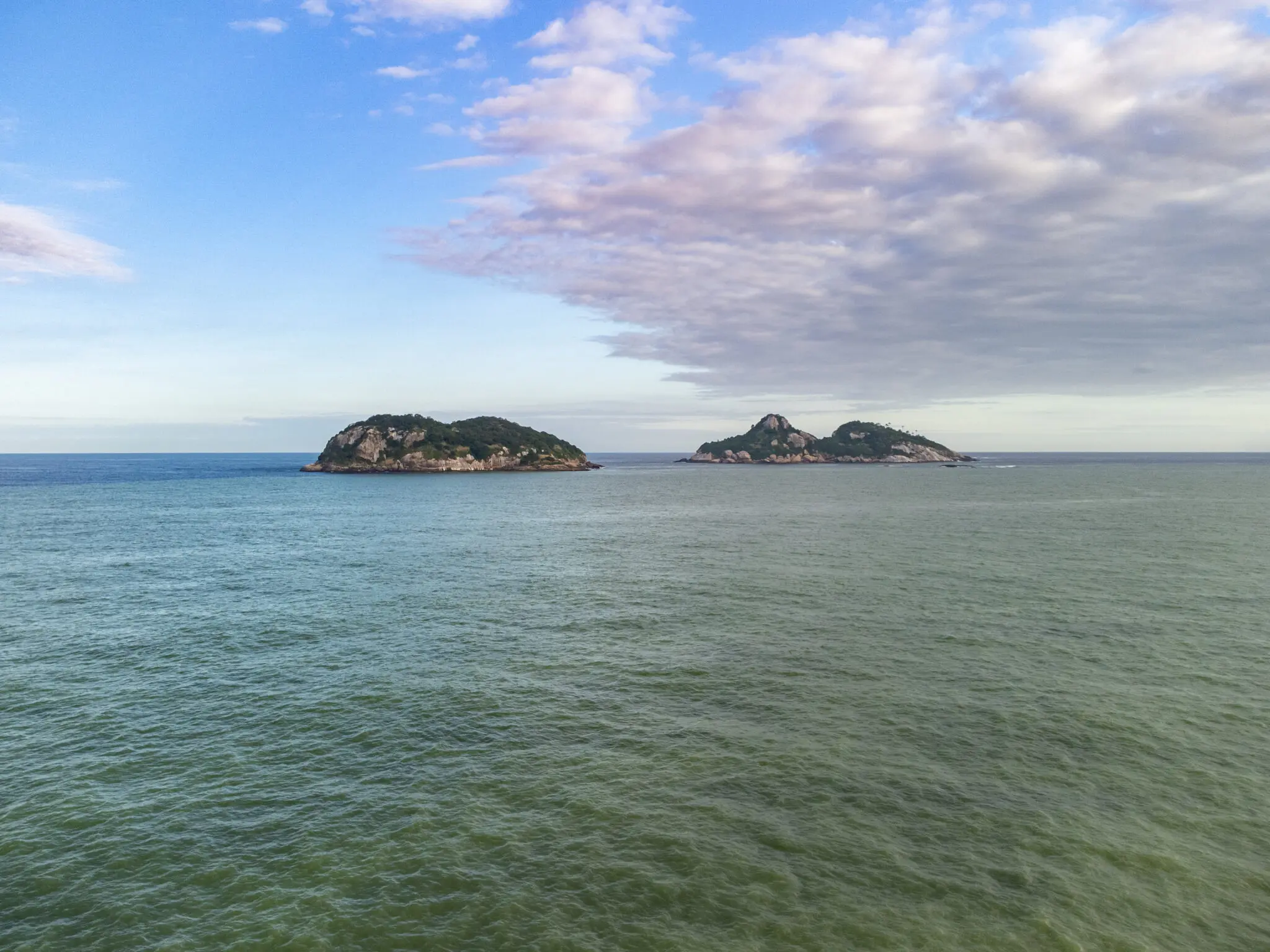 Paisagem marítima com três ilhas verdes e céu azul claro.