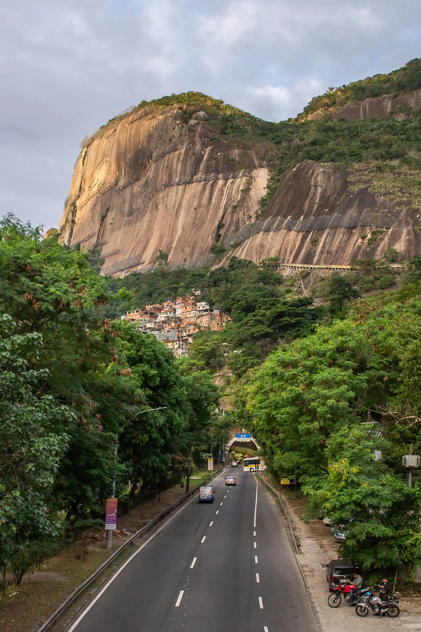 Estrada cortando vale verdejante com formação rochosa imponente ao fundo.