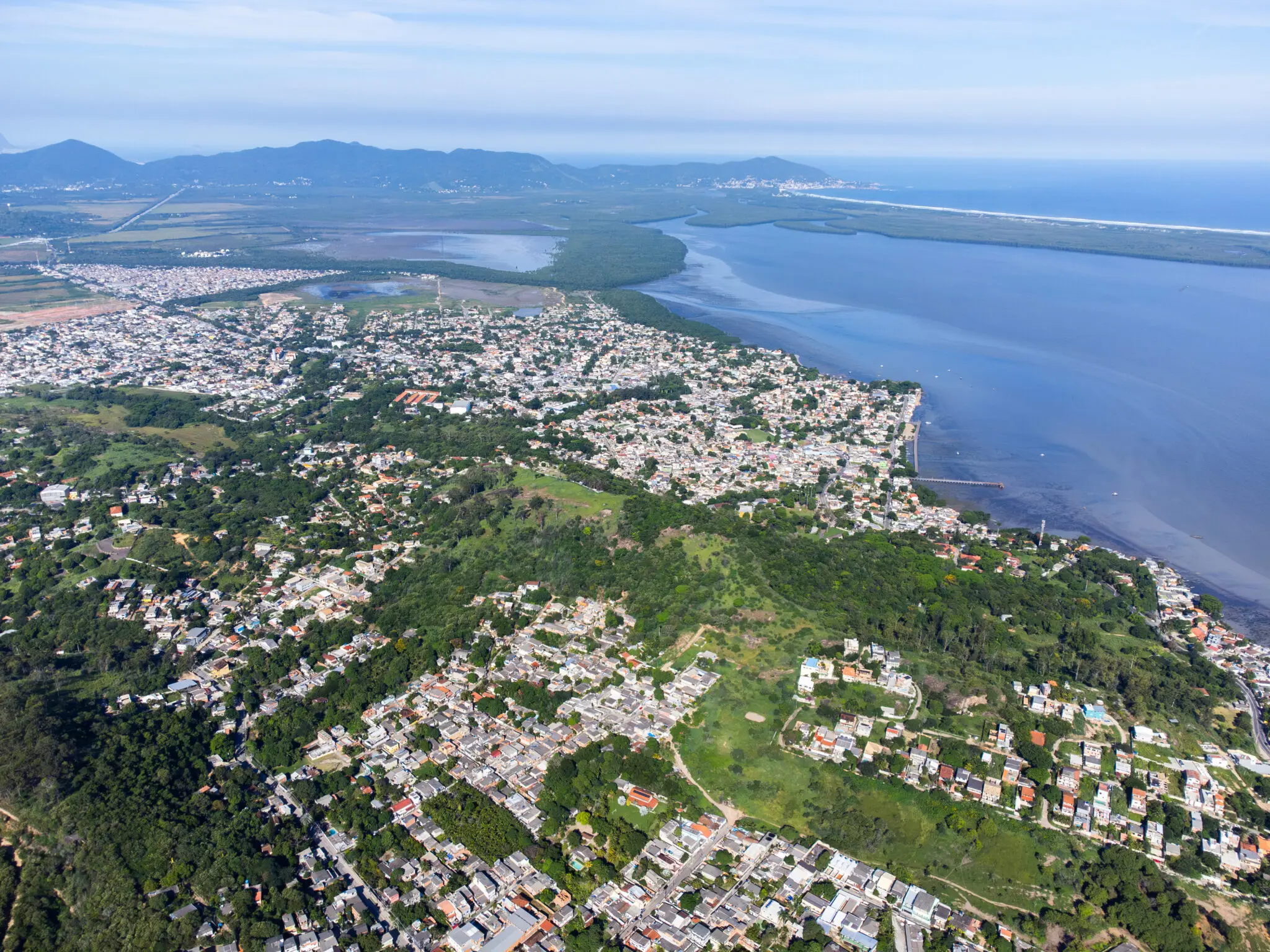 Cidade costeira com áreas verdes e água ao fundo.