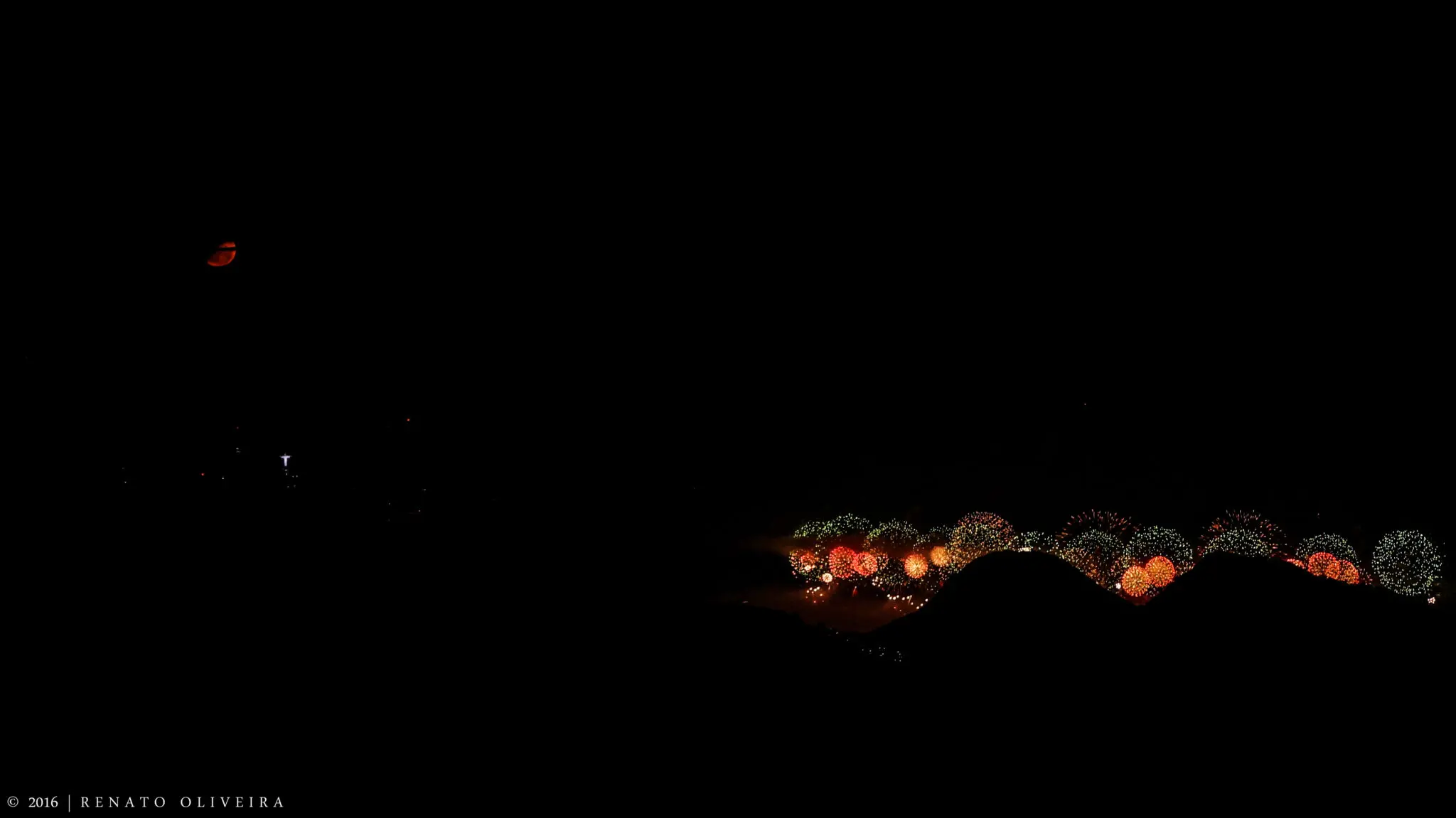 Céu noturno com lua parcial e fogos de artifício coloridos.