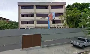 Prédio escolar com placa "Escola Estadual Eunice Weaver", cerca metálica e caminhão cinza.