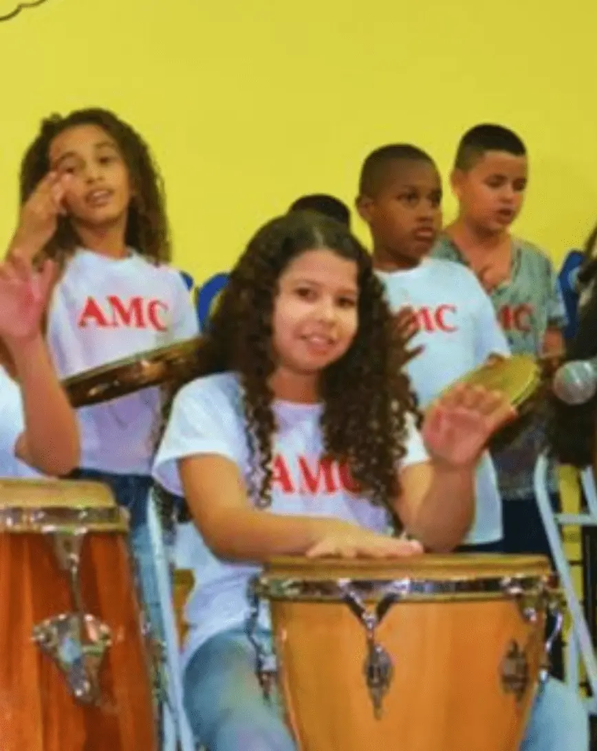 Crianças cantam e tocam instrumentos em apresentação musical.