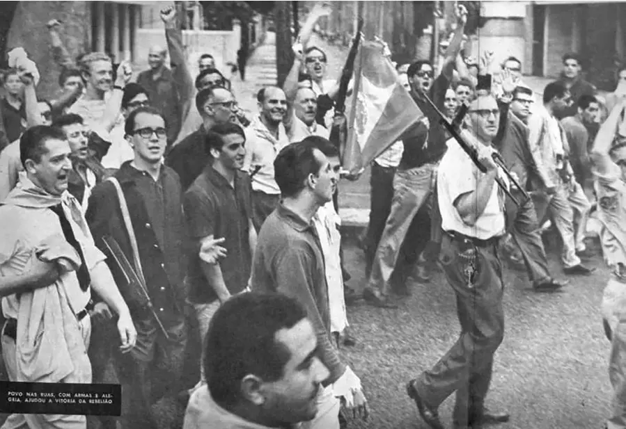 Multidão caminhando pela rua, armas e mãos erguidas.