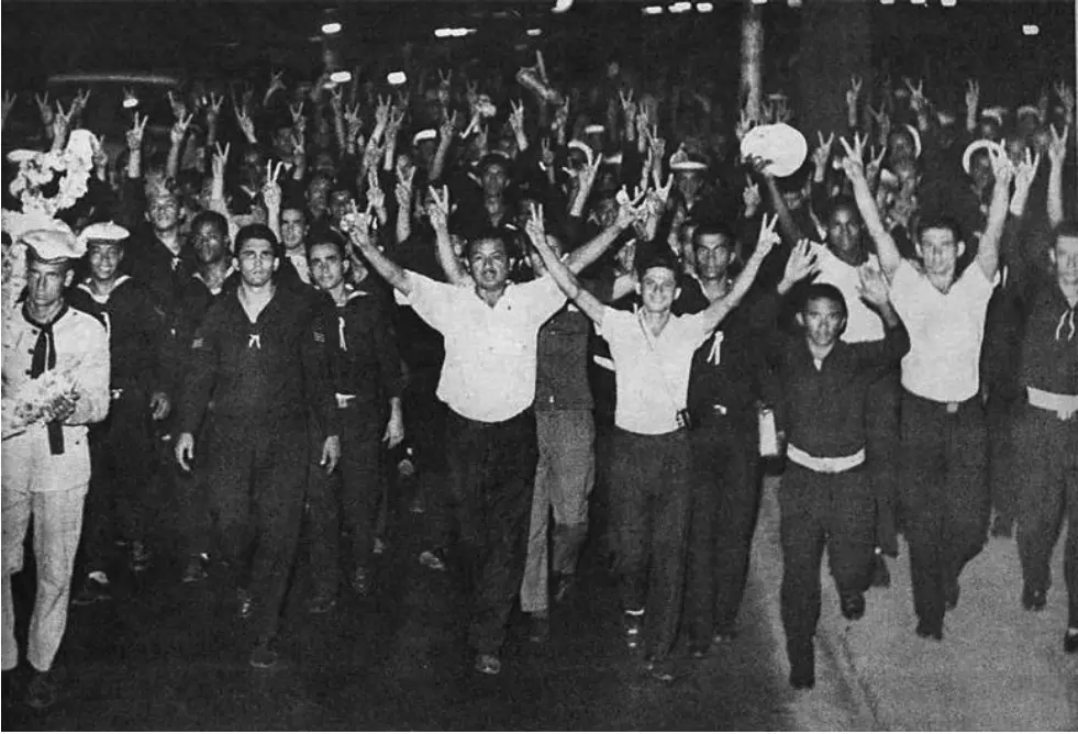 Grupo de pessoas em pé, levantando braços em gestos de paz.