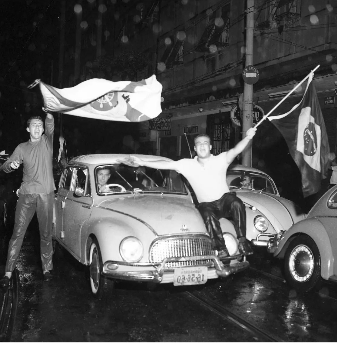 Manifestação noturna urbana com bandeiras sendo agitadas.