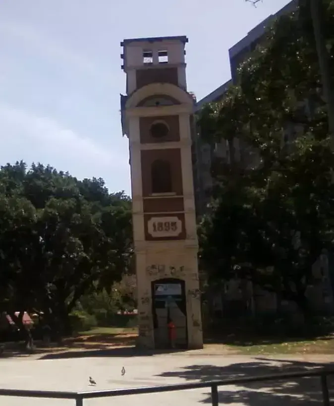 Torre marrom com detalhes brancos em praça, céu azul claro.